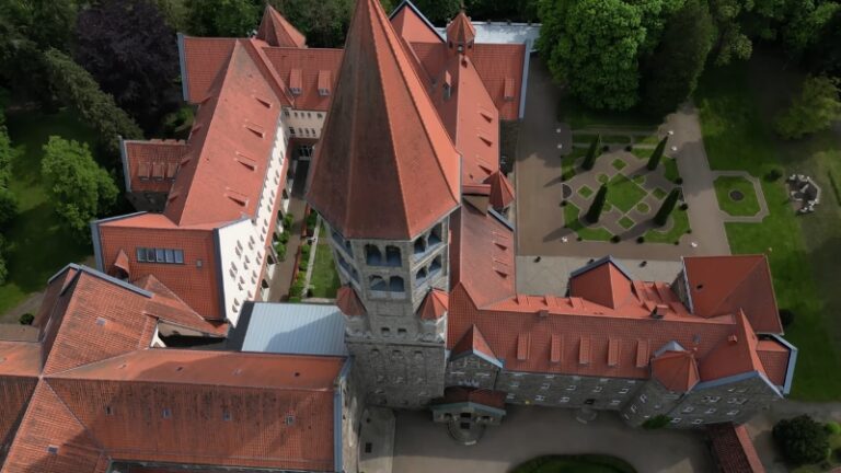 Aerial view of a Swiss church and monastery with a tower and landscaped grounds, one of the churches in Switzerland